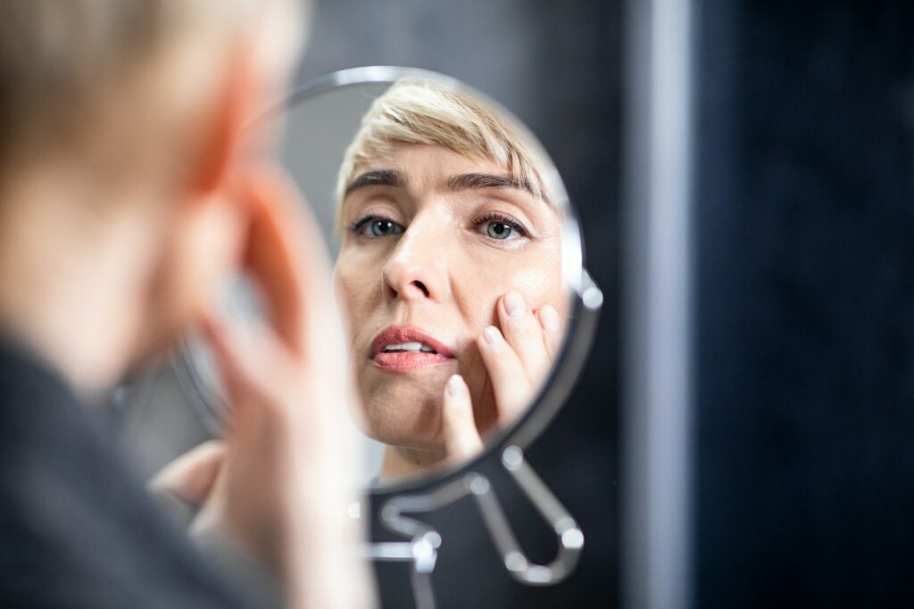 Middle-Aged Lady Looking In Mirror At Wrinkles In Bathroom Indoors